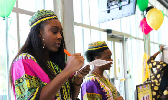 Shani Tracey (left) marks a student’s passport while Jasmine Graham (right) gives a presentation about the popularity of Dashikis in American culture during Monday’s Dashiki Day. 